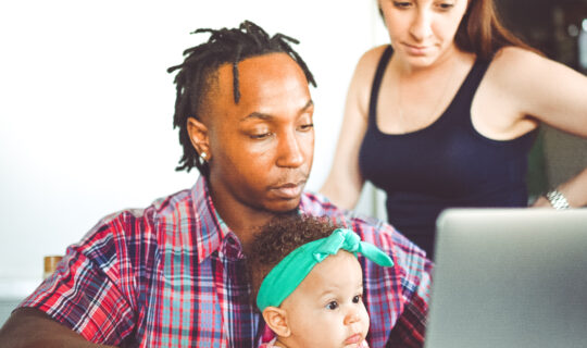 African American dad works on a computer with his infant daughter with mom family using computer